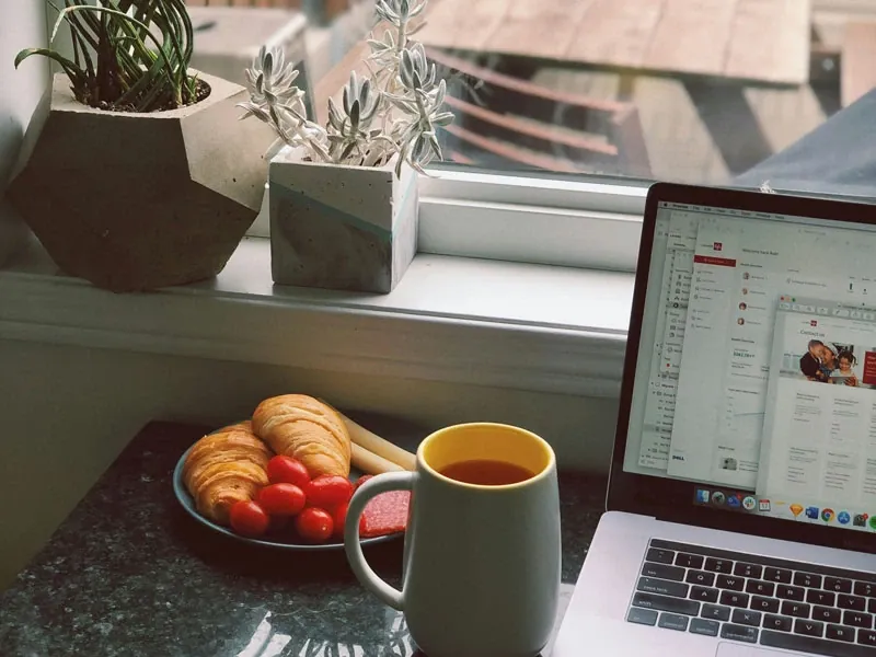 A plate with food, mug, and laptop on a table